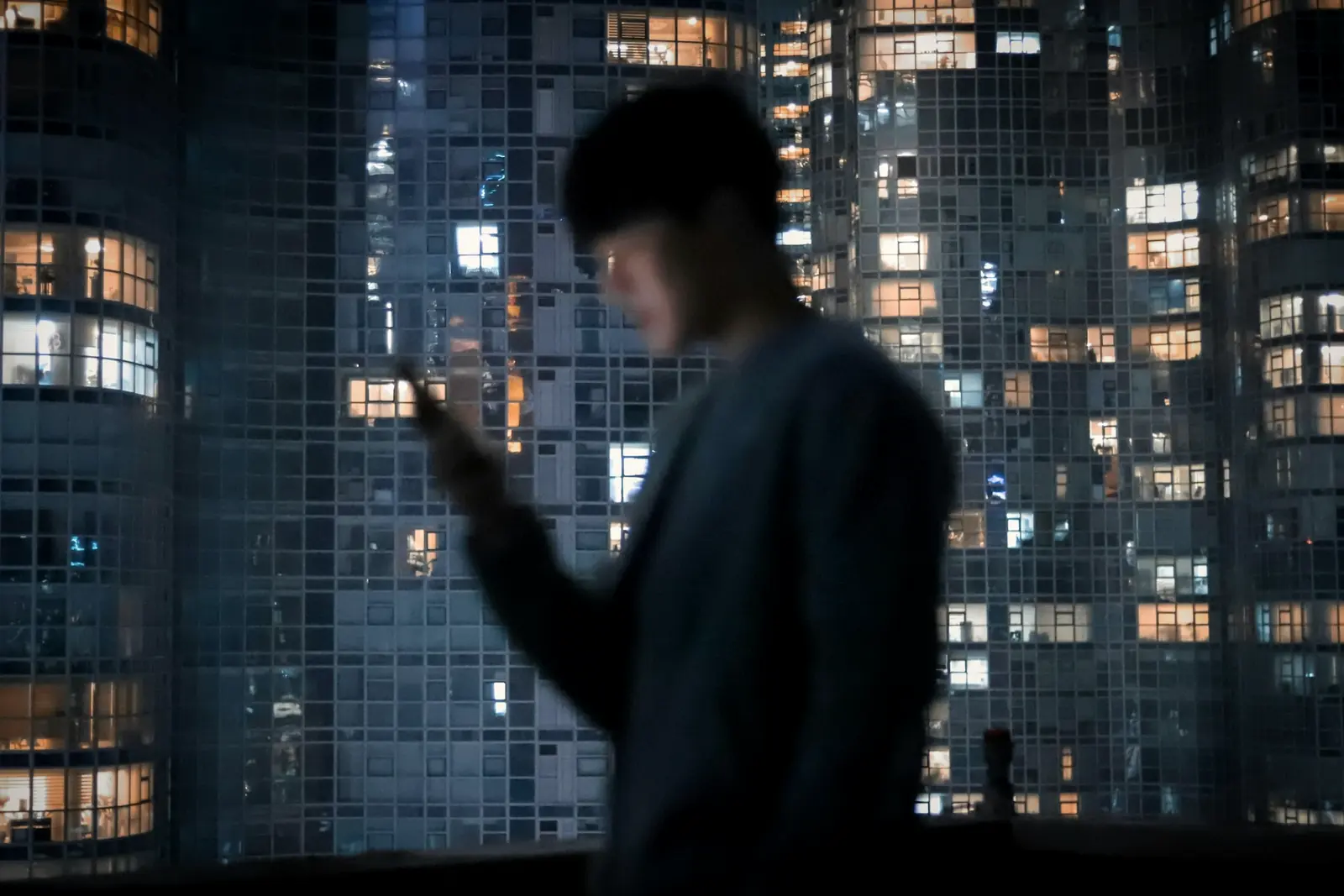 A young man checking his phone by a window full of city lights
