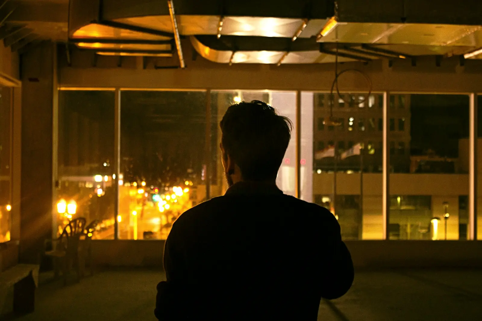 A man looking out of a window at the city at night